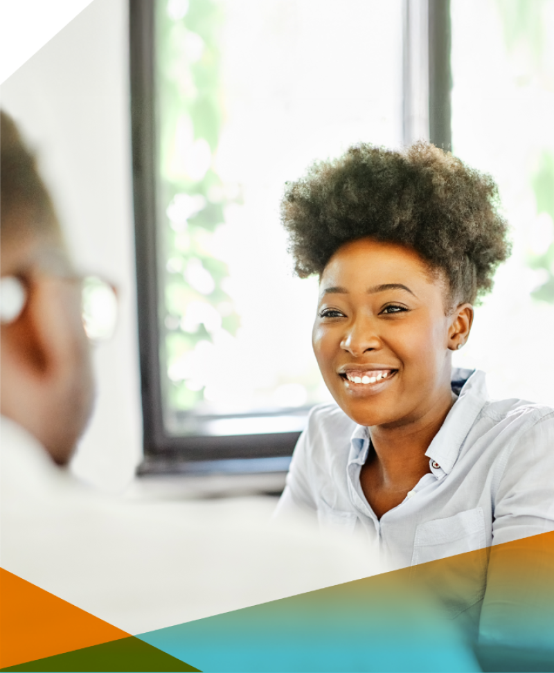 Looking over the shoulder of a man in the foreground he is facing a smiling black woman he is collaborating with.